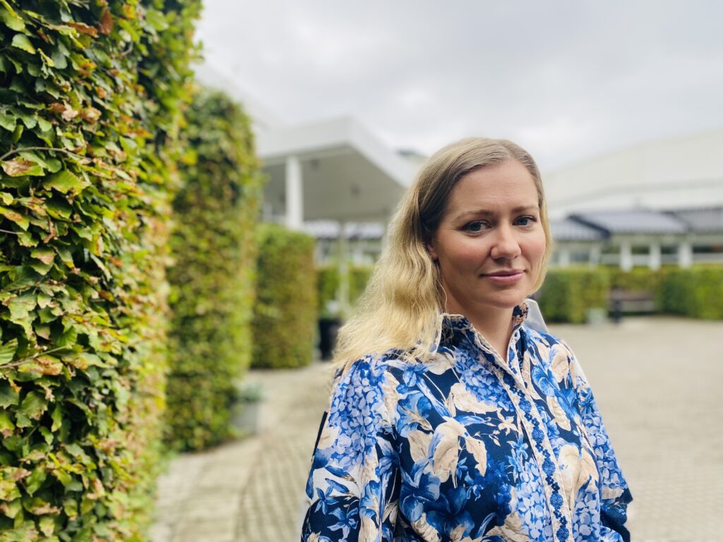 Kvinna står vid buske. Leila McDougal, manusförfattare, producent och skådespelare i Filmen Just a Farmer.